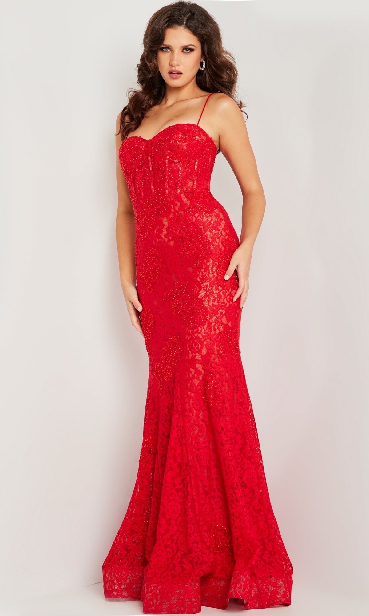 A woman stands against a plain background wearing the Jovani Floor-Length Glitter-Lace Prom Dress 07499 in red, featuring thin straps, a sweetheart neckline, fitted silhouette, and a dramatic mermaid skirt.